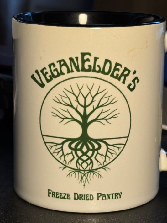 White mug with green tree design logo and 'Veganlder's Freeze Dried Pantry' text in green