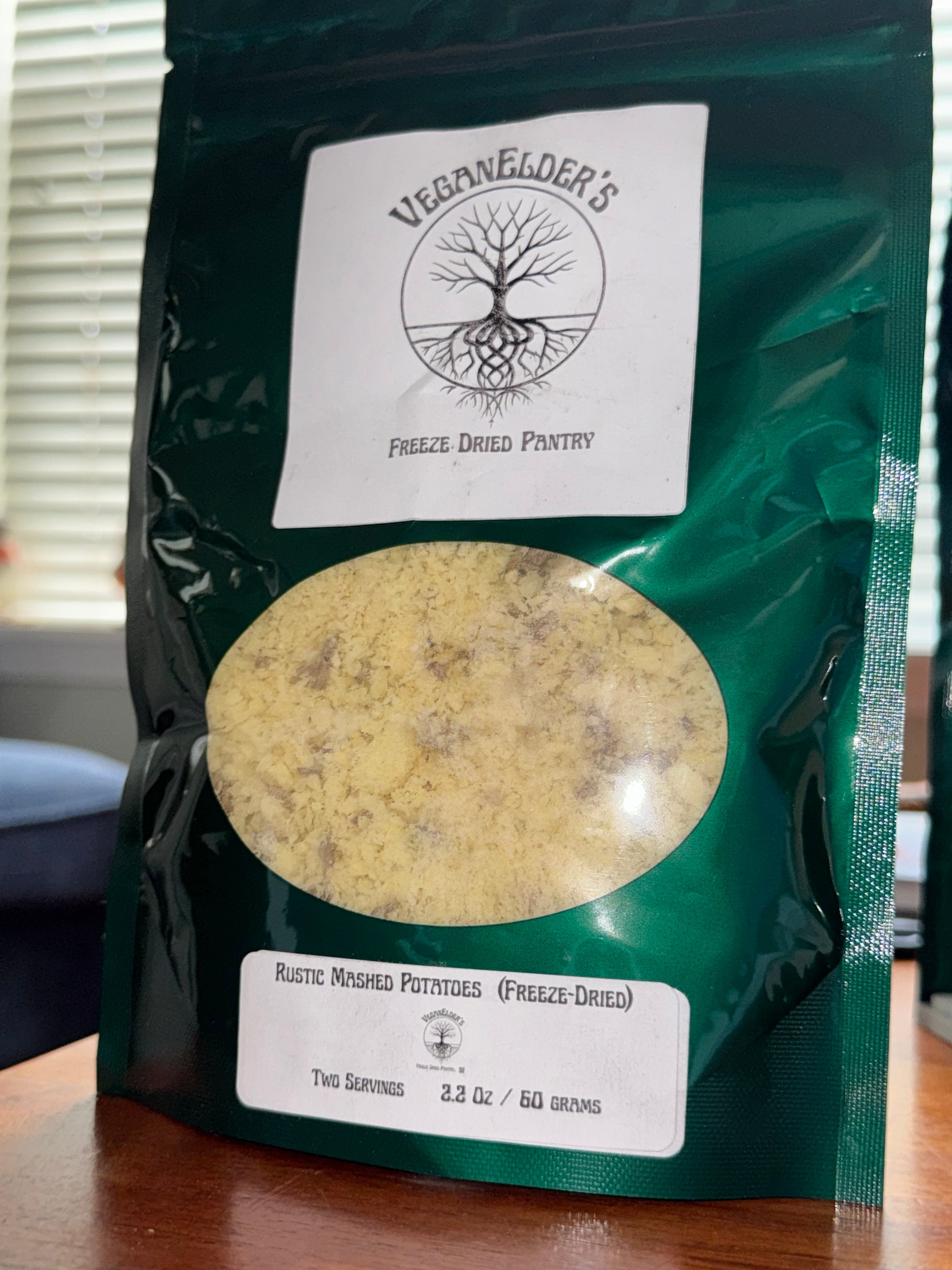 Green package with labels and a round window showing freeze dried mashed potatoes. 