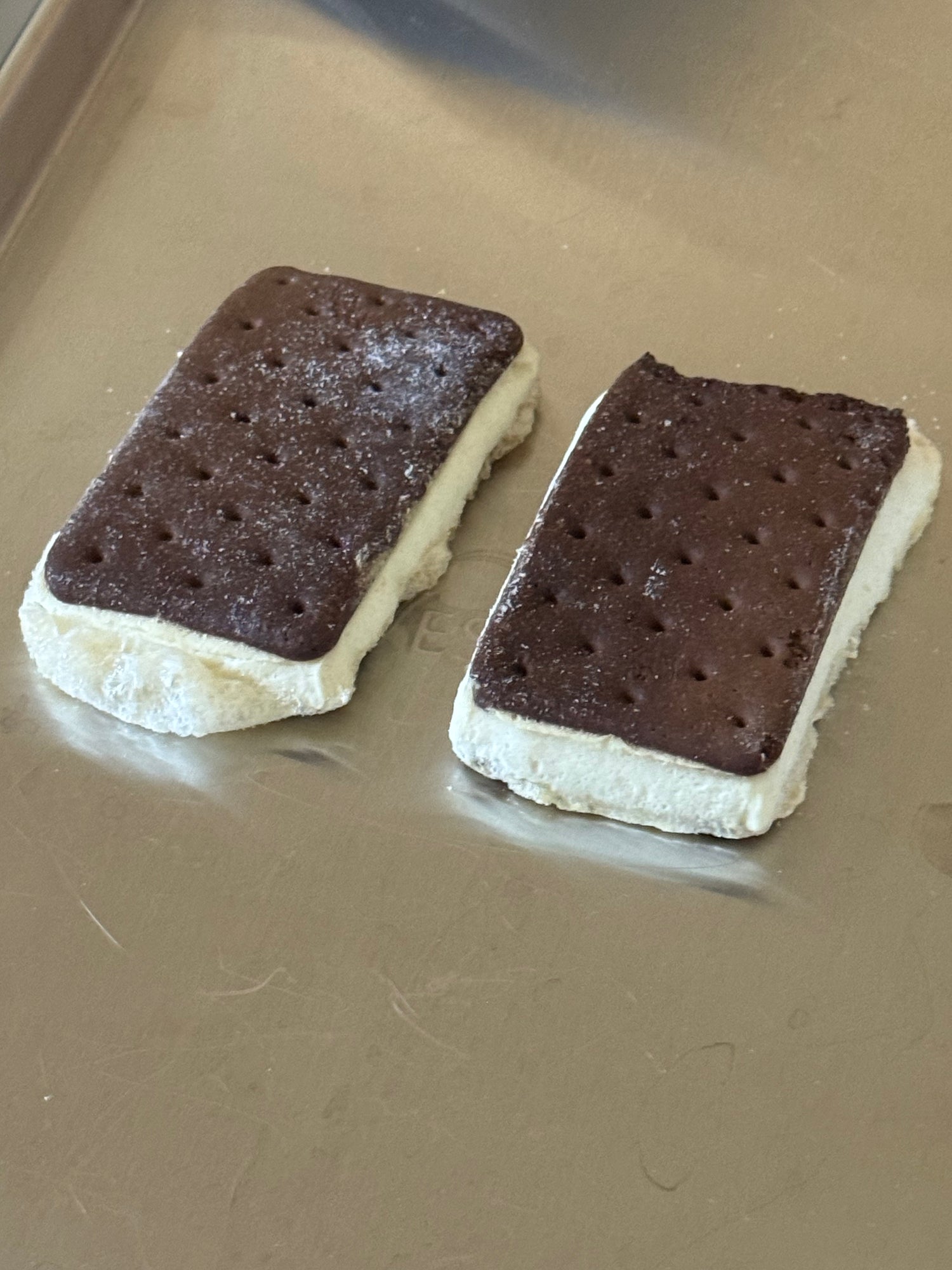 Two ice cream sandwiches with chocolate and vanilla layers on a metal surface.