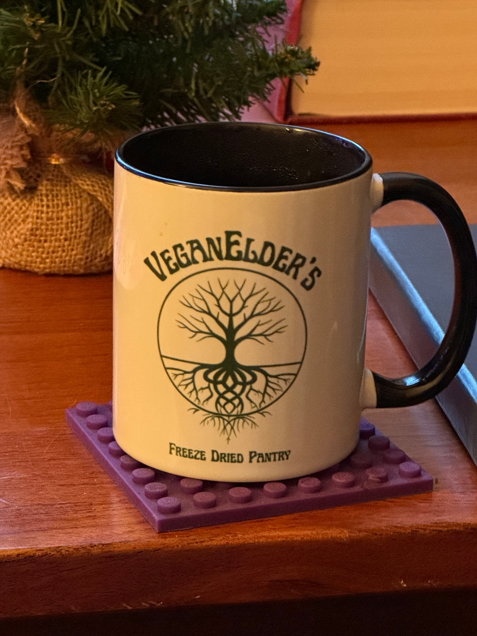 Mug with 'VeganElder's Freeze Dried Pantry' on a purple coaster on a wooden surface.