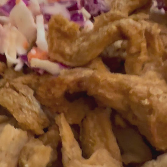 A plate of plant protein strips with tangy barbecue sauce being ladled onto the food for a delicious barbecue meal