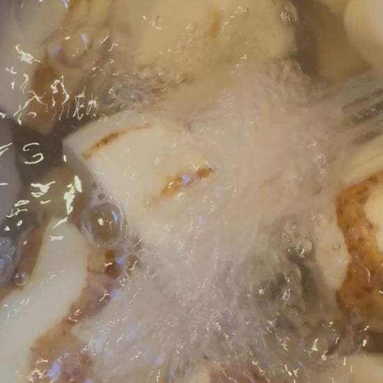 Pot of mostly peeled potatoes with water running over potatoes