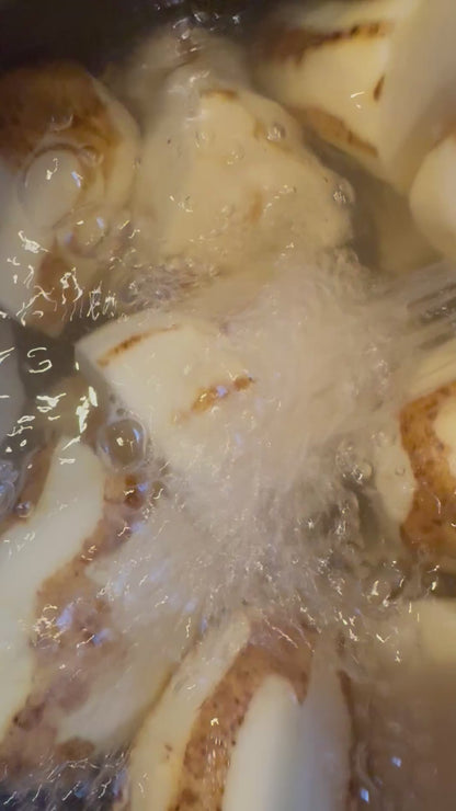 Pot of mostly peeled potatoes with water running over potatoes